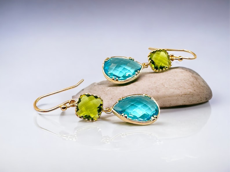 K&ouml;nnte beinhalten: Goldene Ohrh&auml;nger mit einem tropfenf&ouml;rmigen blauen Edelstein und einem quadratischen gr&uuml;nen Edelstein.