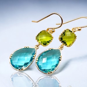K&ouml;nnte beinhalten: Goldene Ohrh&auml;nger mit einem tropfenf&ouml;rmigen blauen Edelstein und einem quadratischen gr&uuml;nen Edelstein.
