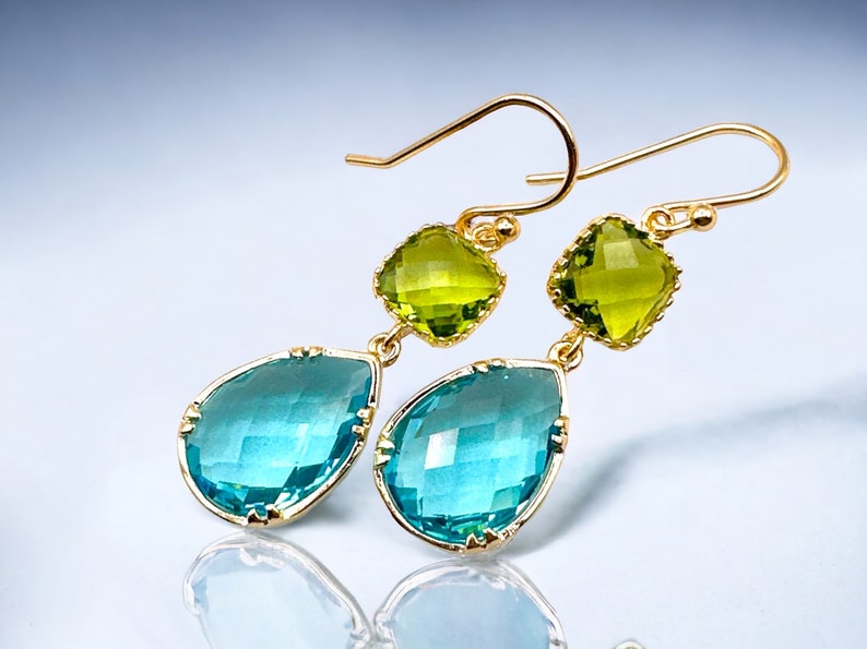 K&ouml;nnte beinhalten: Goldene Ohrh&auml;nger mit einem tropfenf&ouml;rmigen blauen Edelstein und einem quadratischen gr&uuml;nen Edelstein.