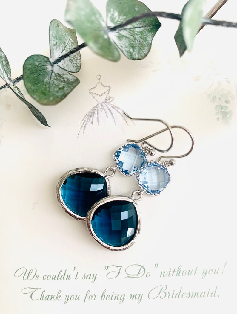 May include: A pair of bridesmaid earrings with a teardrop-shaped dark blue crystal and a smaller light blue crystal. The earrings are silver-toned and have a simple design. The text "We couldn't say "I Do" without you! Thank you for being my Bridesmaid." is written on the card.