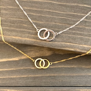 May include: Two delicate necklaces with interlocking circle pendants. One necklace is silver with clear stones, the other is gold with clear stones.