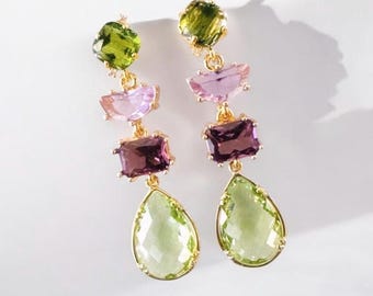 May include: A pair of gold-tone drop earrings featuring a vertical arrangement of four faceted stones: a square olive green stone, a semi-circular light pink stone, a rectangular deep purple stone, and a large pear-shaped light green stone.