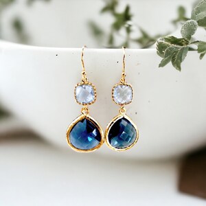 May include: Gold dangle earrings with a teardrop shaped blue crystal and a smaller square shaped clear crystal.