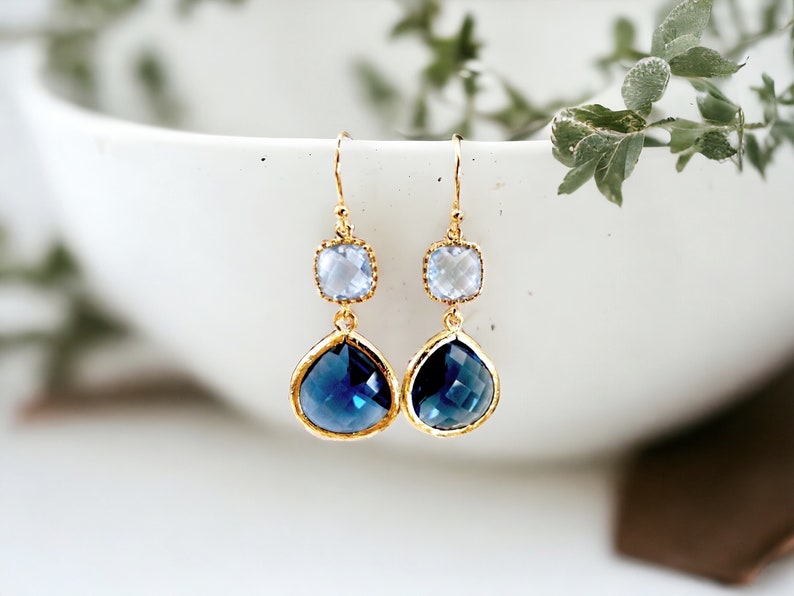 May include: Gold dangle earrings with a teardrop shaped blue crystal and a smaller square shaped clear crystal.