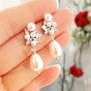Op de afbeelding: Een paar zilveren oorhangers met een cluster van kleine parels en strass steentjes, en een grotere parel druppel.