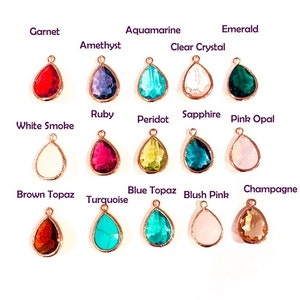 May include: A collection of teardrop-shaped gemstone pendants in various colors, including garnet, amethyst, aquamarine, and emerald. Each gem is set in a rose gold-colored metal frame, with the name of each stone printed above it.