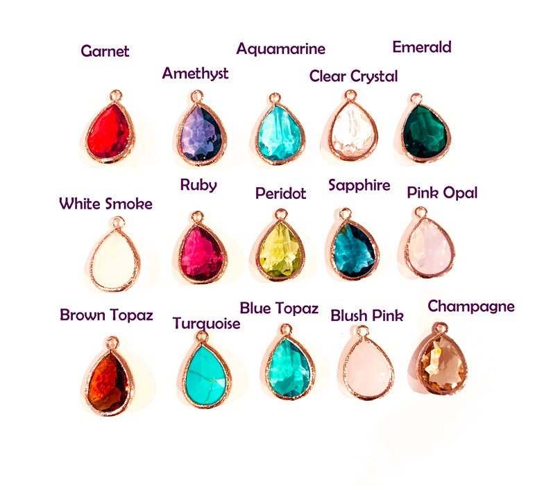 May include: A collection of teardrop-shaped gemstone pendants in various colors, including garnet, amethyst, aquamarine, and emerald. Each gem is set in a rose gold-colored metal frame, with the name of each stone printed above it.
