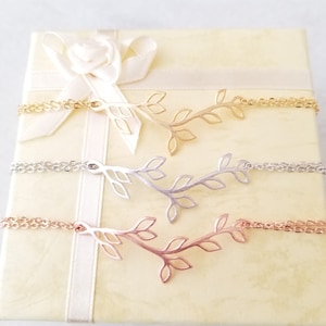 May include: Three delicate gold, silver, and rose gold necklaces with a branch and leaf design. The necklaces are displayed in a white and gold gift box with a white satin ribbon.