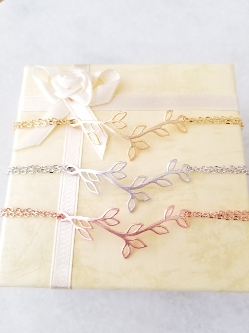 May include: Three delicate gold, silver, and rose gold necklaces with a branch and leaf design. The necklaces are displayed in a white and gold gift box with a white satin ribbon.