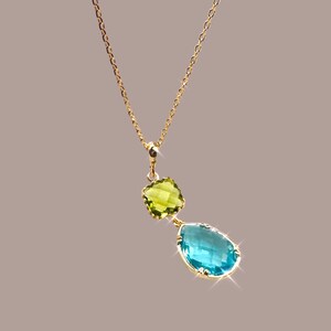 K&ouml;nnte beinhalten: Eine goldene Kettenkette mit einem Anh&auml;nger, der einen tropfenf&ouml;rmigen blauen Edelstein und einen kleineren quadratischen gr&uuml;nen Edelstein zeigt.