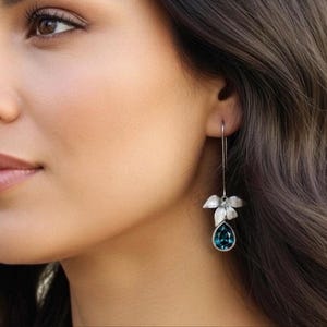 May include: A silver-toned earring with a leaf design and a teardrop-shaped teal gemstone. The earring hangs from a thin wire, showcasing a delicate and elegant style. The jewelry is a beautiful accessory.