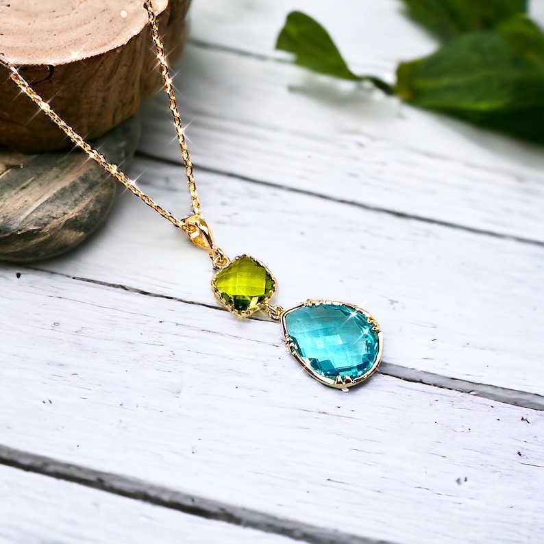 K&ouml;nnte beinhalten: Eine goldene Kettenkette mit einem tropfenf&ouml;rmigen blauen Kristallanh&auml;nger und einem kleineren gr&uuml;nen Kristallanh&auml;nger.