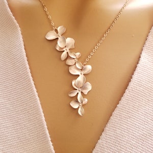 May include: A gold-colored necklace featuring a cascade of stylized flower pendants. The floral design is delicate and detailed, with each petal subtly textured. The necklace hangs on a fine chain, creating an elegant and feminine accessory.