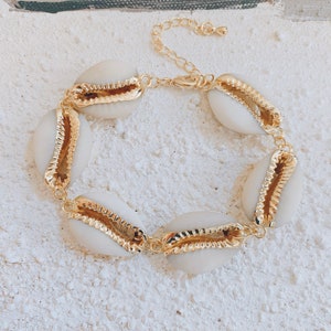 May include: A gold chain bracelet with white seashells. The seashells have a gold trim around the edges.