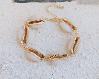 Puede incluir: Un brazalete de cadena dorada con conchas blancas. Las conchas tienen un borde dorado.