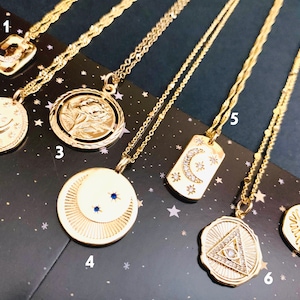 May include: Seven gold necklaces with different pendants, including a crescent moon, a rose, a crescent moon with stars, a triangle with an eye, a sun with an eye, and a crescent moon with stars. The necklaces are on a black background with gold stars.