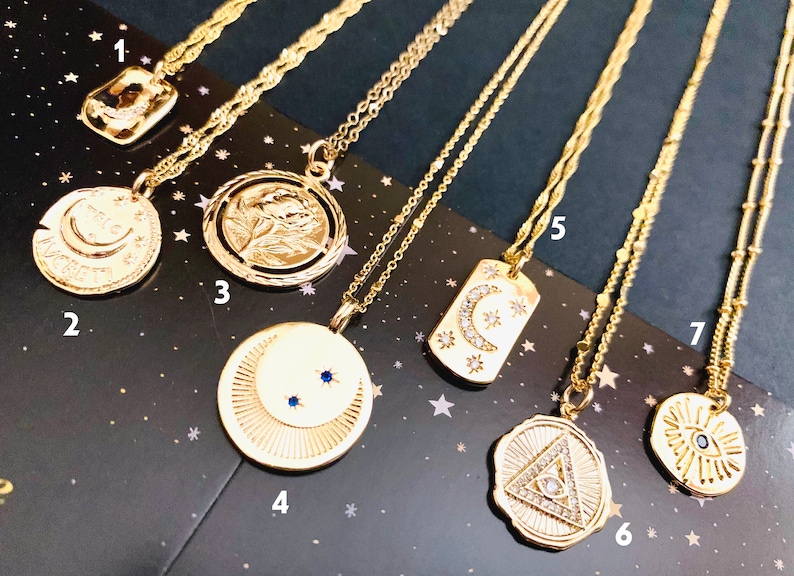 May include: Seven gold necklaces with different pendants, including a crescent moon, a rose, a crescent moon with stars, a triangle with an eye, a sun with an eye, and a crescent moon with stars. The necklaces are on a black background with gold stars.