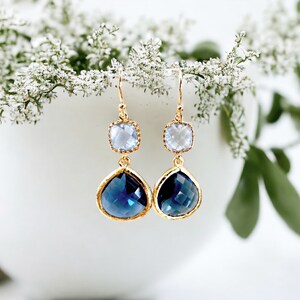 May include: Gold dangle earrings with a teardrop shaped blue crystal and a smaller square clear crystal.