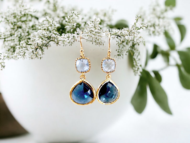 May include: Gold dangle earrings with a teardrop shaped blue crystal and a smaller square clear crystal.