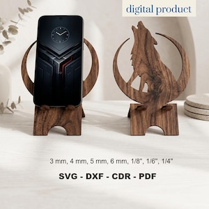 May include: Two dark brown wooden phone stands featuring a cutout of a howling wolf against a crescent moon. One stand holds a smartphone with a clock face display. Text includes digital product, 3 mm, 4 mm, 5 mm, 6 mm, 1/8", 1/6", 1/4", SVG, DXF, CDR, PDF.
