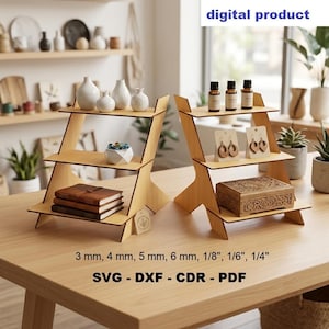May include: Two three-tiered light wood display stands on a table. The left stand holds white vases, a small bowl, and notebooks. The right stand holds essential oil bottles, earring cards, and a carved box. Text reads: digital product, 3 mm, 4 mm, 5 mm, 6 mm, 1/8", 1/6", 1/4", SVG, DXF, CDR, PDF.