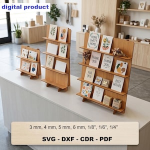 Puede incluir: Tres expositores escalonados de madera clara para tarjetas y objetos pequeños. Los expositores cuentan con varios estantes y se muestran con diversas tarjetas de felicitación y pequeños objetos decorativos. El texto incluye 3 mm, 4 mm, 5 mm, 6 mm, 1/8", 1/6", 1/4", SVG, DXF, CDR, PDF.