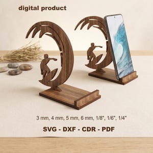 Puede incluir: Dos soportes de madera marrón oscuro para teléfono con un diseño recortado de un surfista sobre una ola. El texto digital product, 3 mm, 4 mm, 5 mm, 6 mm, 1/8", 1/6", 1/4" y SVG - DXF - CDR - PDF es visible. Un soporte sostiene un smartphone.