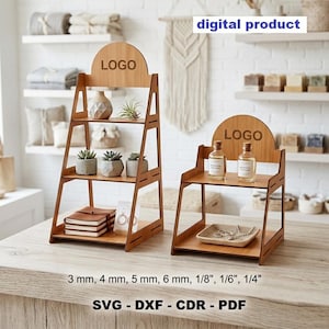 以下が含まれることがあります： LOGOという文字が入ったアーチ型のトップを持つ、明るい茶色の木製段付きディスプレイスタンド2つ。背の高いスタンドには棚が3段、低いスタンドには棚が2段あります。下部のテキストには3 mm, 4 mm, 5 mm, 6 mm, 1/8", 1/6", 1/4" および SVG - DXF - CDR - PDF と記載されています。
