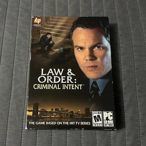 Può includere: Una custodia per gioco PC CD-ROM di Law & Order: Criminal Intent. La copertina presenta un ritratto di un uomo in giacca e cravatta, una scena più piccola di una persona accovacciata in un vicolo e uno skyline notturno. Il logo ESRB M è visibile.