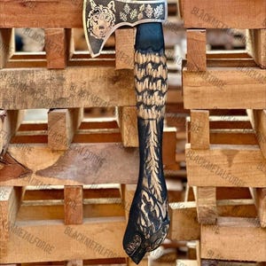 May include: A metal axe featuring a silver-toned blade engraved with a wolf head and leaf patterns. The handle is crafted from dark wood with intricate, carved feather-like textures running down its length, ending in a sculpted animal head base.