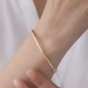 Op de afbeelding: Een gepolijste goudkleurige armband met een glad, afgerond oppervlak. De armband heeft een eenvoudig, doorlopend cirkelvormig ontwerp dat comfortabel om de pols rust en een reflecterende metalen afwerking laat zien.