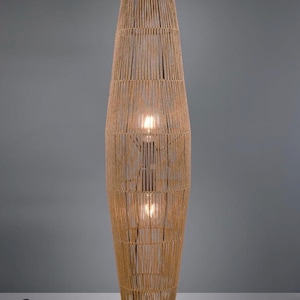 Peut inclure: Un lampadaire cylindrique haut doté d'un enroulement de corde en fibre naturelle brun clair autour d'une structure métallique. La lampe contient deux ampoules visibles à travers les brins de corde verticaux et repose sur une base circulaire noire.