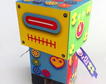 May include: A colorful papercraft robot with a yellow head, blue body, and red, green, and purple accents. The robot has a heart-shaped design on its chest and a purple ribbon with a zig-zag pattern on its back. The robot is part of a printable kit.
