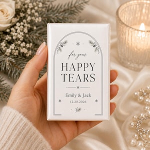 May include: A rectangular white wedding tissue packet featuring a black arched frame design with pine branch illustrations, snowflakes, and the text "for your HAPPY TEARS", "Emily & Jack", and the date "20.12.2026" printed in a serif font.