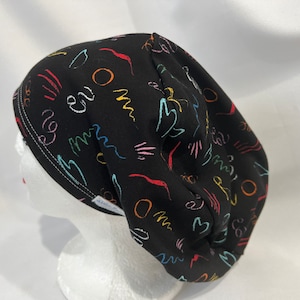 May include: Black scrub hat with a colorful abstract doodle pattern. The hat has a white drawstring and a white label with the word "Alana" on it.