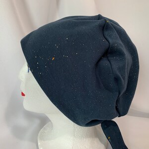 May include: A dark blue beanie with a sparkly finish. The beanie has a long tie that can be tied under the chin.