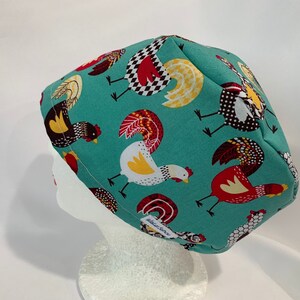 May include: Teal blue scrub hat with a pattern of colorful roosters. The hat has a white elastic band.