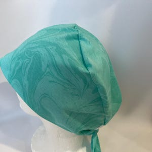 May include: A turquoise blue surgical scrub hat with a marbled pattern. The hat has a tie at the back.