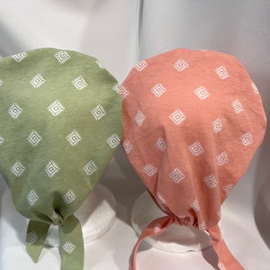 May include: Two fabric headbands with a white geometric pattern on a light green and a light pink background. The headbands are tied at the back.
