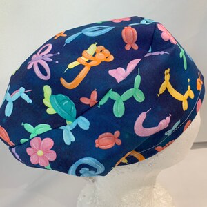 May include: A blue scrub hat with a colorful balloon animal print. The hat has a tie on the back.