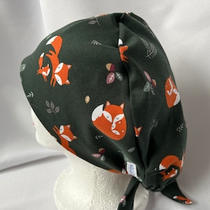 May include: A dark green scrub hat with a repeating pattern of orange foxes and leaves. The hat has a tie at the back.