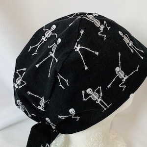 May include: Black scrub hat with a white skeleton pattern. The hat has a tie at the back.