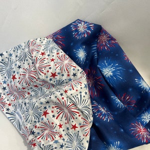 May include: Two fabric squares with a white background and red and blue firework patterns. One square has a blue background with white and red fireworks. The other square has a white background with red stripes and white stars.