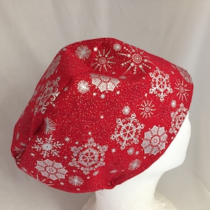 May include: Red scrub hat with a white snowflake pattern. The hat is made of a soft, comfortable fabric and has a tie closure.