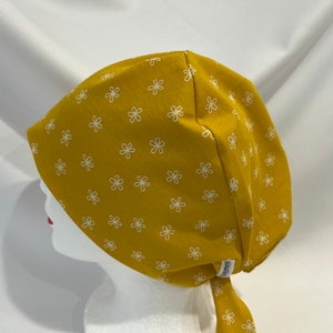 May include: A yellow scrub hat with a white daisy pattern. The hat has a tie at the back.