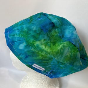 May include: A blue and green tie-dye scrub hat with white stitching and a small white label that says "All About Scrubs".