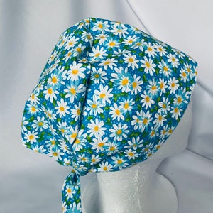 May include: A blue and white floral scrub hat with a white daisy pattern. The hat has a tie at the back.