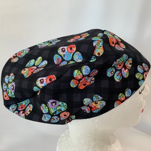 May include: Black scrub hat with a paw print pattern featuring colourful flowers. The hat has a black and white checkered background.