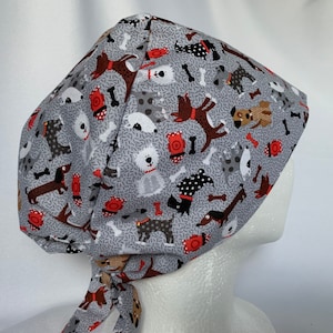 May include: Gray surgical scrub cap with a repeating pattern of various dog breeds, bones, and red fire hydrants. The cap is tied at the back and is designed to cover the hair during medical procedures.