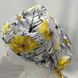 May include: A floral patterned head covering featuring large yellow and gray flowers on a white background. The design includes black accents. The head covering is tied at the back.